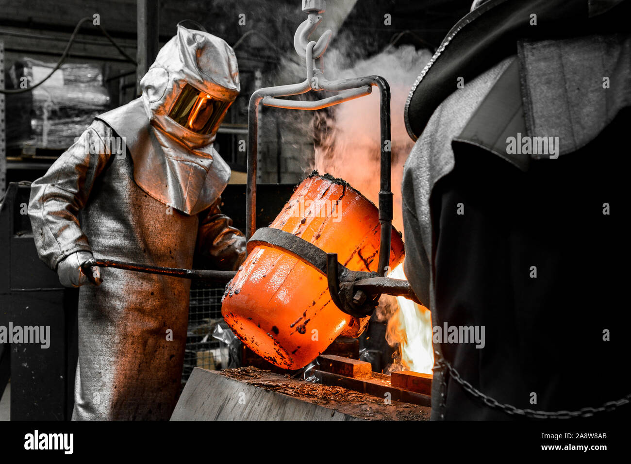 In una fonderia officina. Un lavoratore protetto da una tuta di sicurezza versa il metallo fuso in uno stampo Foto Stock