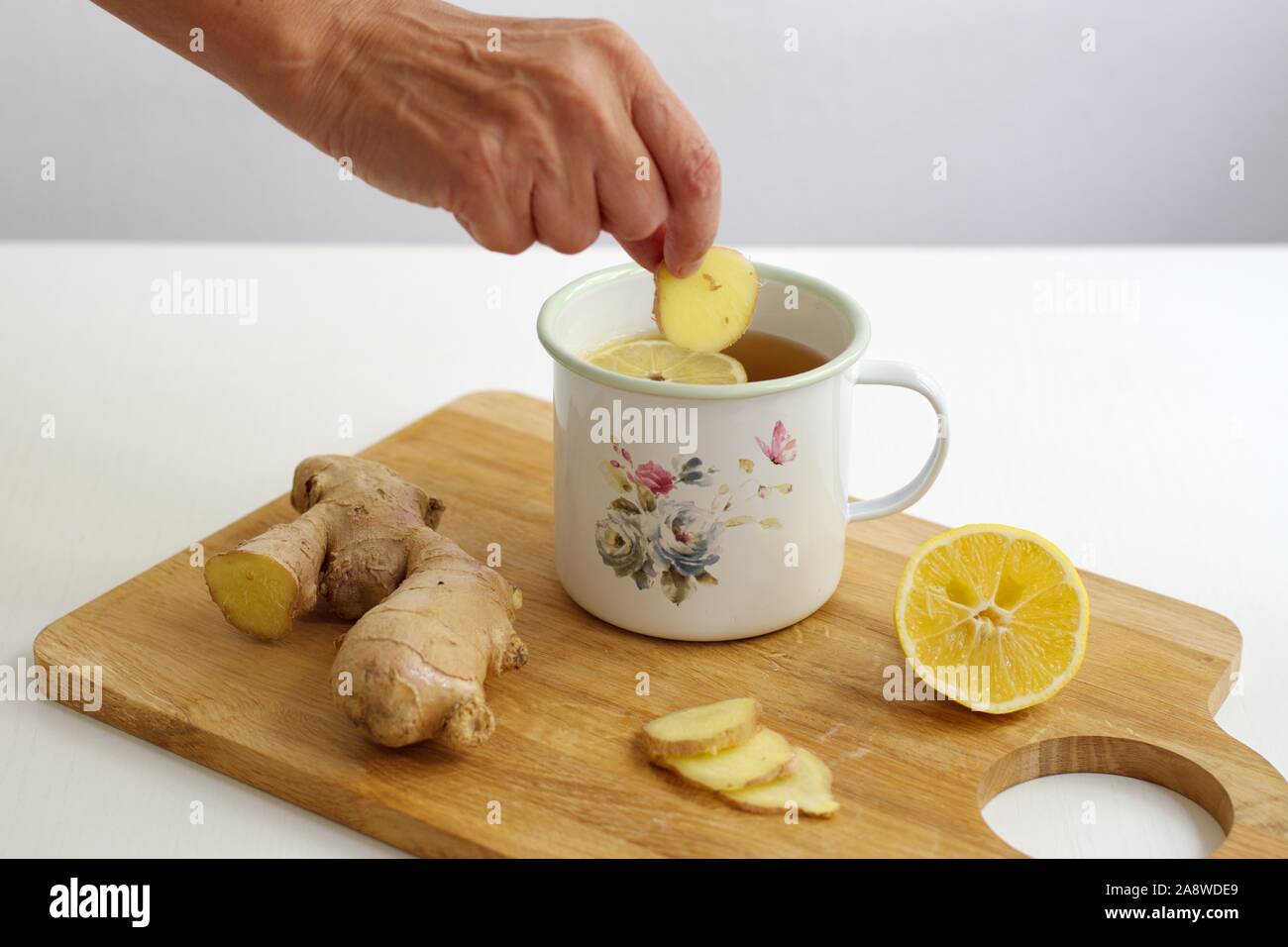 Closeup colpo di zenzero e tè allo zenzero con il limone nel contenitore decorativo - donna di mano che tiene lo zenzero Foto Stock