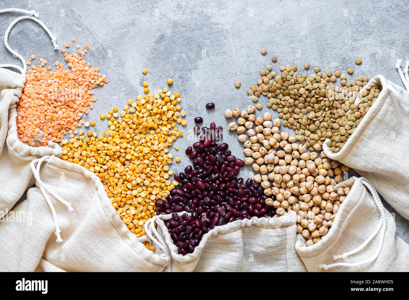 Diversi legumi in sacchetti di eco. Lenticchie, fagioli, piselli, ceci sono sparse su sfondo grigio. Lay piatto con posto per il testo. Foto Stock