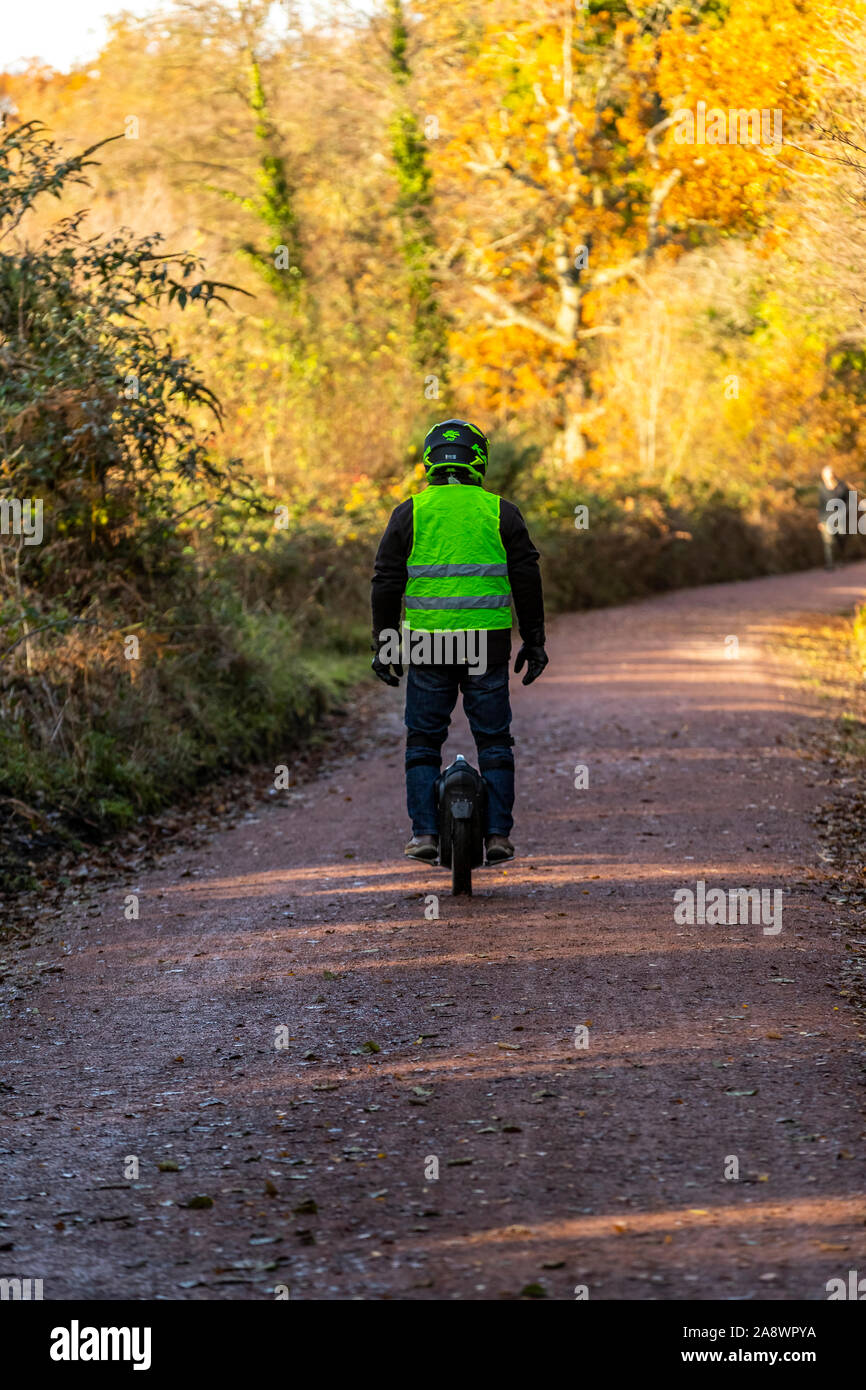 Un uomo che cavalca un monociclo elettrico lungo una ex ferrovia linea adesso un cycleway a Cannop stagni, Foresta di Dean. Autunno Foto Stock