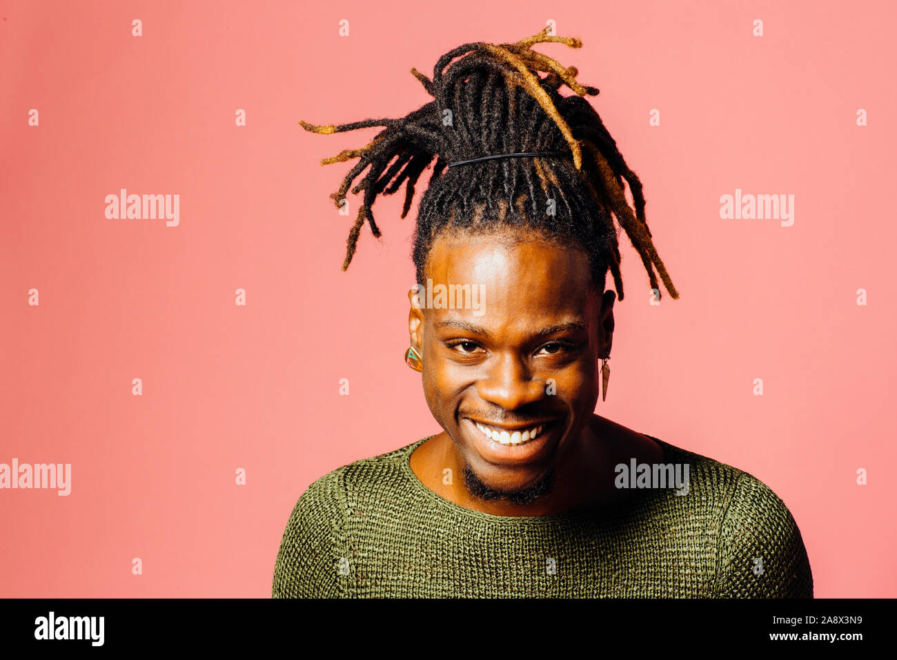 Ritratto di un felice, sorridente giovane con cool dreadlocks acconciatura guardando la telecamera, isolato in rosa Foto Stock
