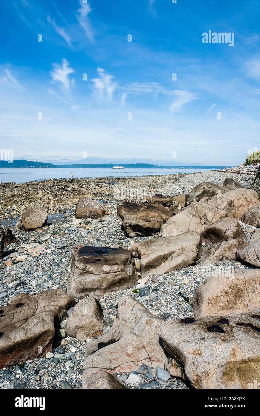Rocky Alki Beach con una donna sola sulla riva e un traghetto in Puget Sound a ovest di Seattle, Washington. Foto Stock