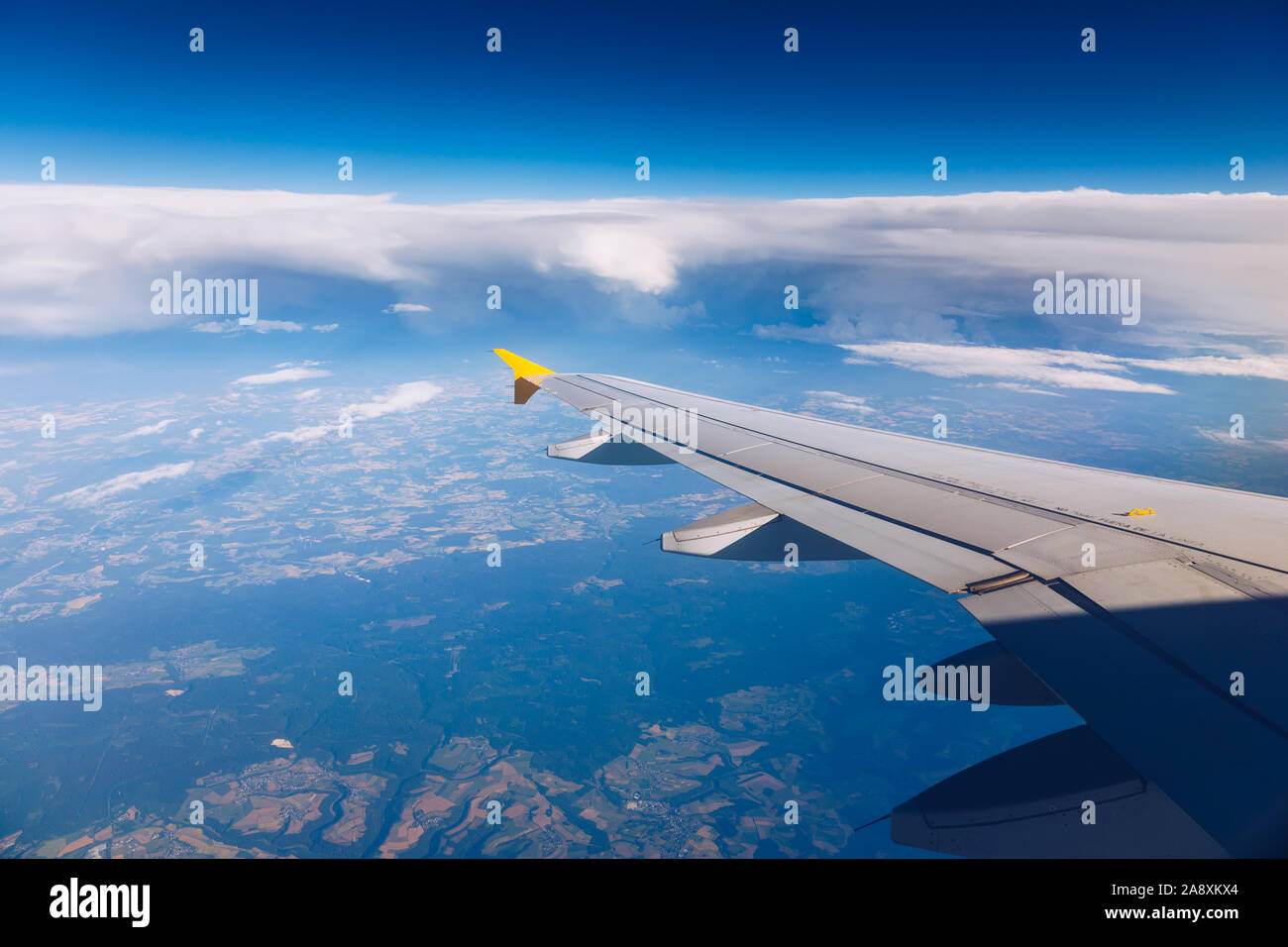 Vista di un'ala di aeroplano che vola sopra le nuvole ad alta altitudine sotto un cielo blu dall'alzavetro passeggero. In volo sopra l'Europa. Vista di je Foto Stock