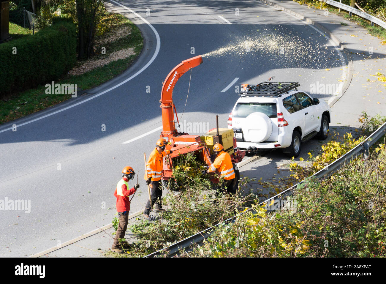 Maienfeld, GR / Svizzera - 11 Novembre 2019: città equipaggio di manutenzione con una cippatrice e shredder chiara e pulita spallamento stradale della vegetazione Foto Stock