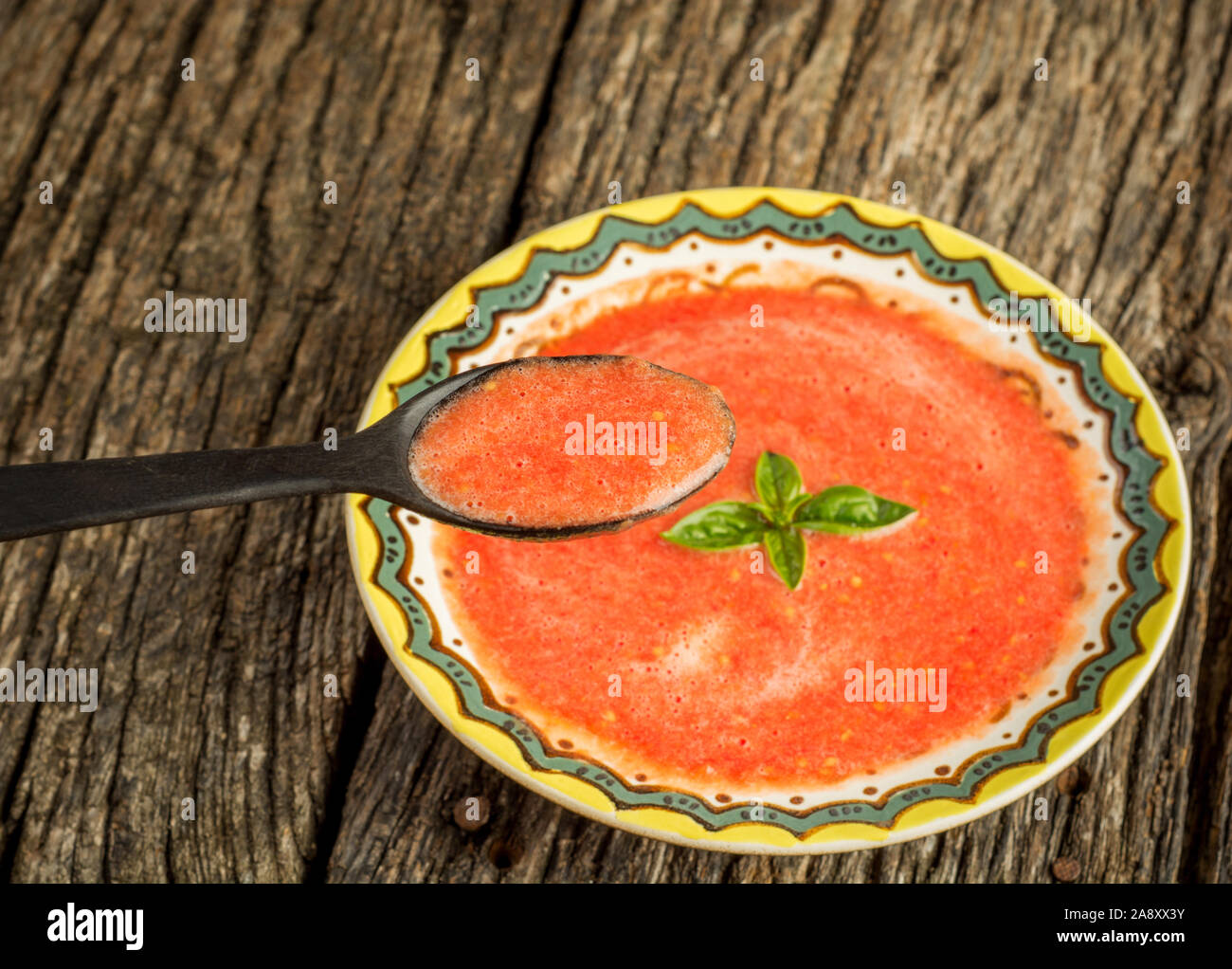 Zuppa Gazpacho con il verde del basilico in vaschetta di colore giallo su sfondo rustico. Spagnolo tradizionale zuppa fredda purea. Lay piatto. Foto Stock