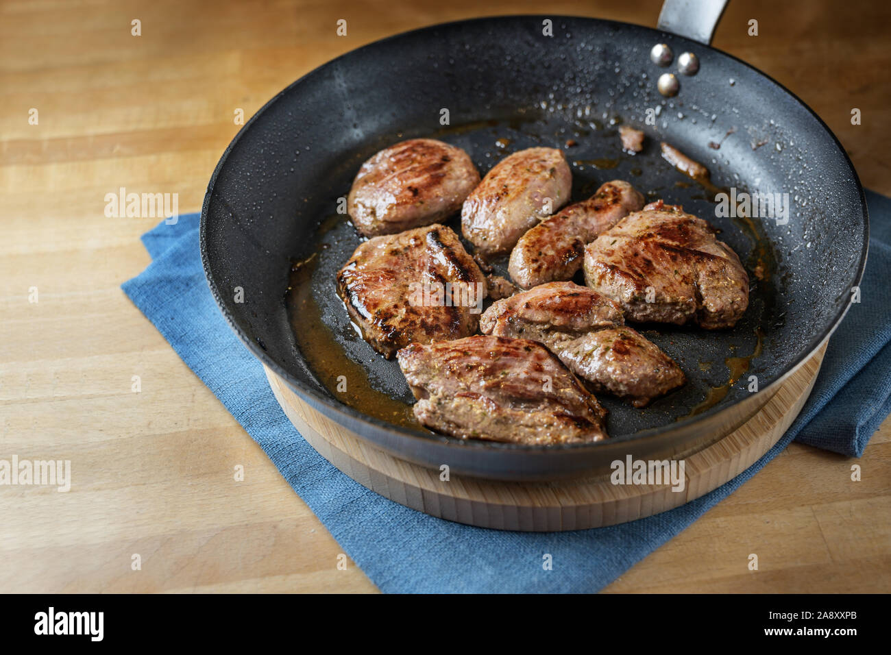 Succosa di filetti di agnello appena fritte in padella e servita su una tavola di legno, spazio copia selezionata, focus, profondità di campo ridotta Foto Stock