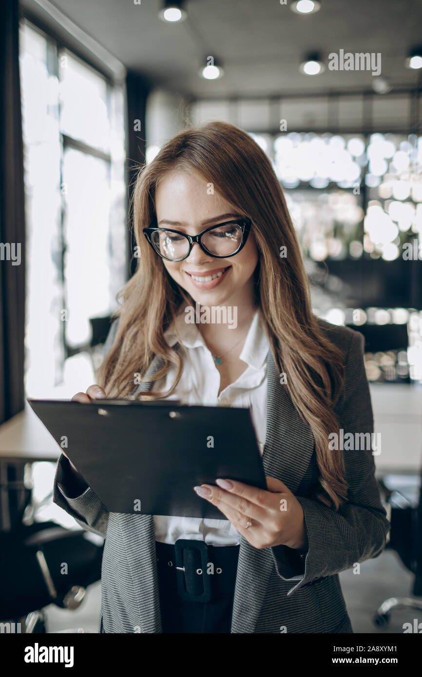 Bellissima femmina dipendente ufficio in bicchieri sorridente e guardarla negli appunti di Windows Foto Stock