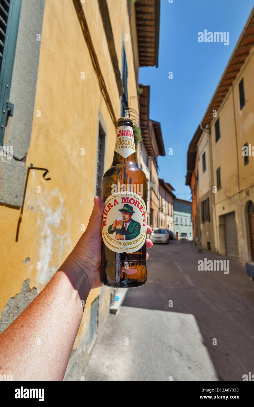 MONTOPOLI, Italia - Luglio 24, 2019: bianco uomo mano trattiene un Moretti birra italiana, antica strada in background. Montopoli in Val d'Arno è un municipali Foto Stock