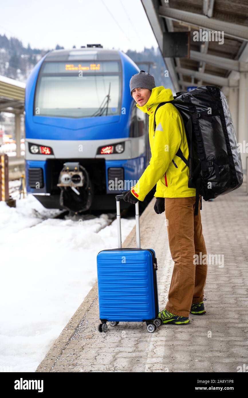 Per turisti in cerca di fotocamera con valigia blu alla stazione in attesa del treno contro sullo sfondo di montagne sulla giornata invernale Foto Stock