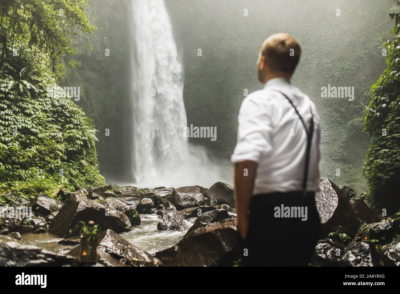 Viaggiatore uomo cerca su enorme cascata Nung-Nung in Bali Jungle. Asia concetto di viaggio. Vista incredibile. Foto Stock