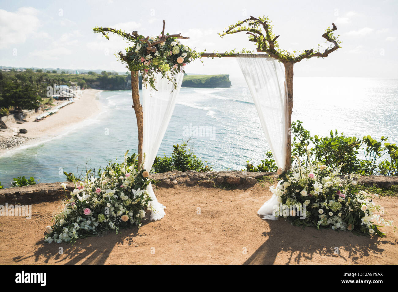 Tramonto cerimonia di nozze arch con rami in legno e decorazioni floreali e panno bianco baldacchino. Vista della scogliera Balangan in Bali. Nozze con vista oceano. Foto Stock