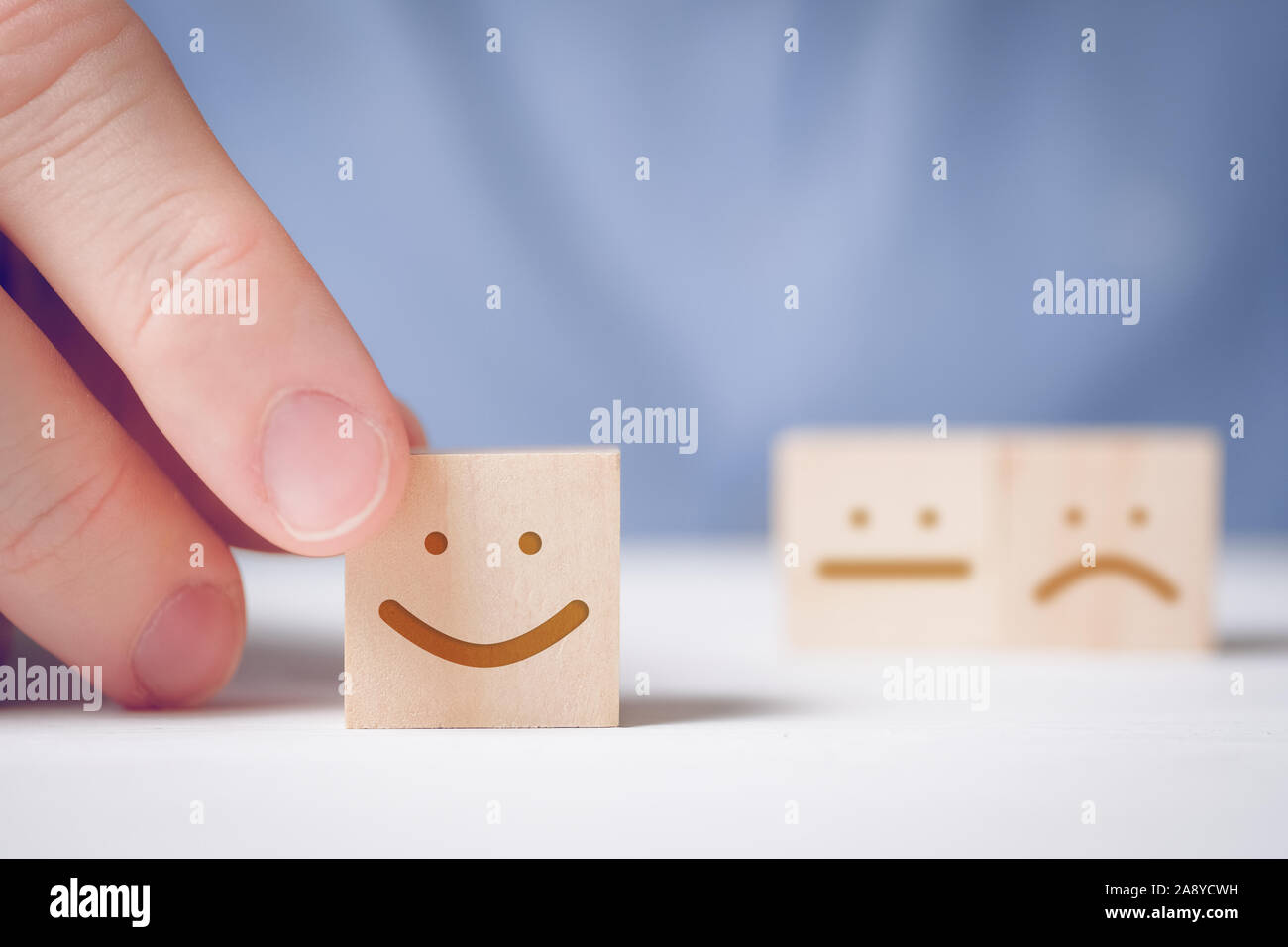 Un uomo detiene un cubo di legno con un volto positivo su una posizione neutrale e sfondo negativo. Concetto per la valutazione di un'azione o una risorsa. Close up. Foto Stock
