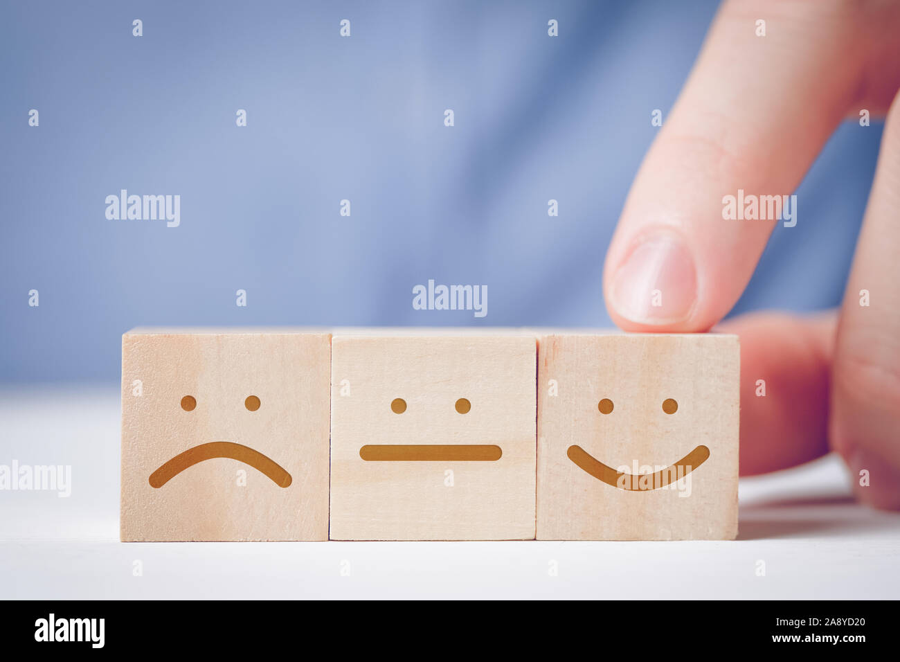 Un uomo di punta il dito in corrispondenza di un cubo di legno con un volto positivo accanto a una folle e dispiaciuto. Concetto per la valutazione di un'azione o una risorsa. Close up Foto Stock