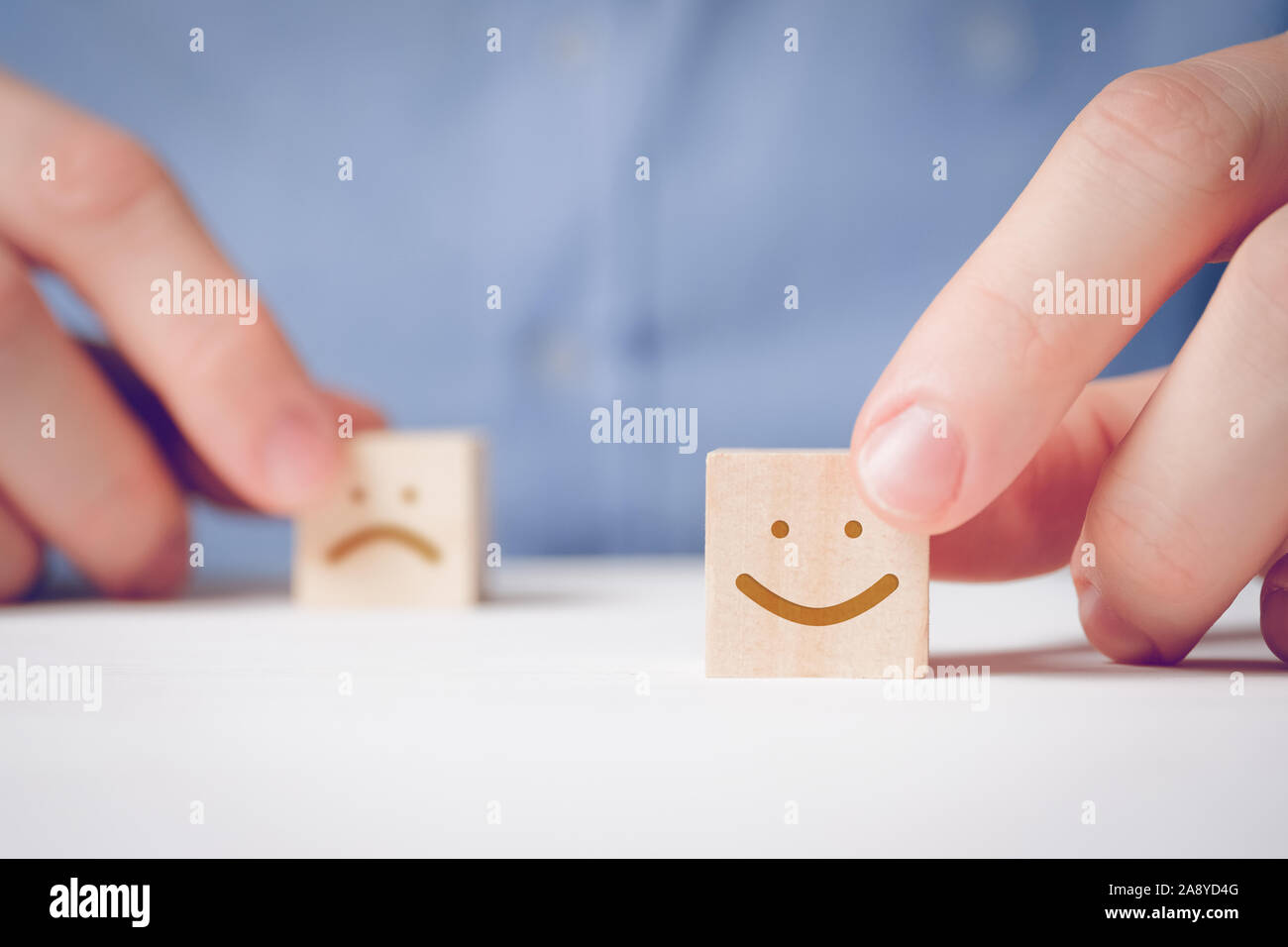 Un uomo tiene con le sue dita di un cubo di legno con un volto positivo accanto a un uno insoddisfatti. Concetto per la valutazione di un'azione o una risorsa. Close up. Foto Stock