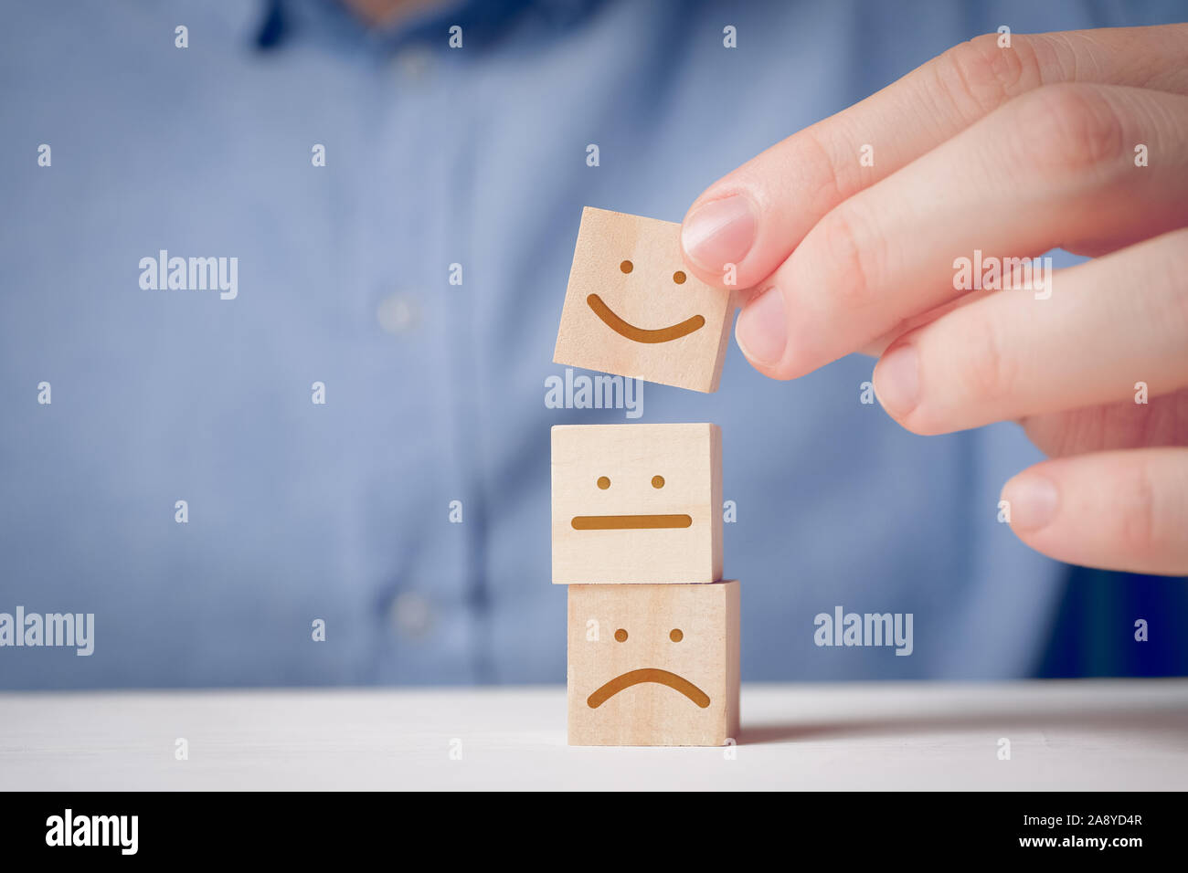 Un uomo tiene con le sue dita di un cubo di legno con un volto positivo accanto a un scontenti e neutro. Concetto per la valutazione di un'azione o una risorsa. C Foto Stock