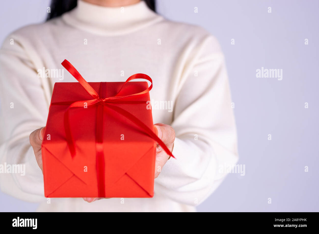 Primo piano delle mani dando confezione regalo. La donna le consegne in rosso di un pacchetto regalo con un nastro rosso. Holiday/ compleanno/ concetto di Natale banner. Foto Stock