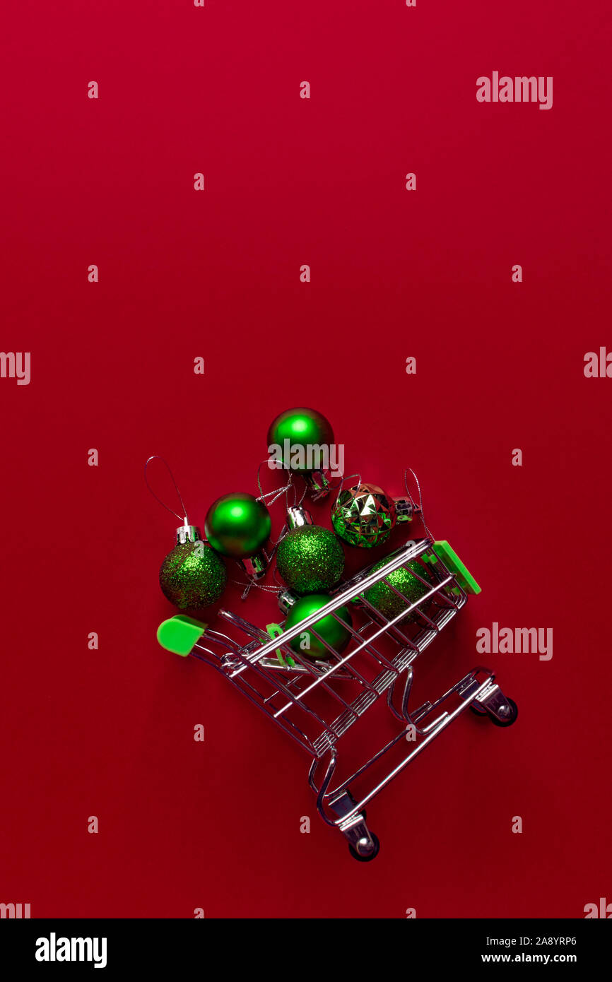 Un piccolo carrello di metallo da un supermercato riempito con il verde dei giocattoli di Natale si trova su uno sfondo di colore rosso. Giocattoli ottenere abbastanza sonno da un cestello.concep trading Foto Stock