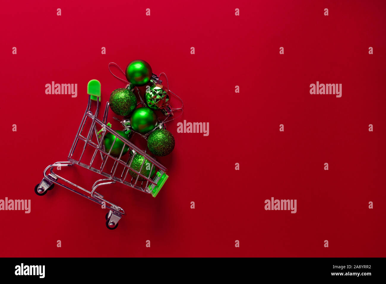 Un piccolo carrello di metallo da un supermercato riempito con il verde dei giocattoli di Natale si trova su uno sfondo di colore rosso. Giocattoli ottenere abbastanza sonno da un cestello. Ph orizzontale Foto Stock