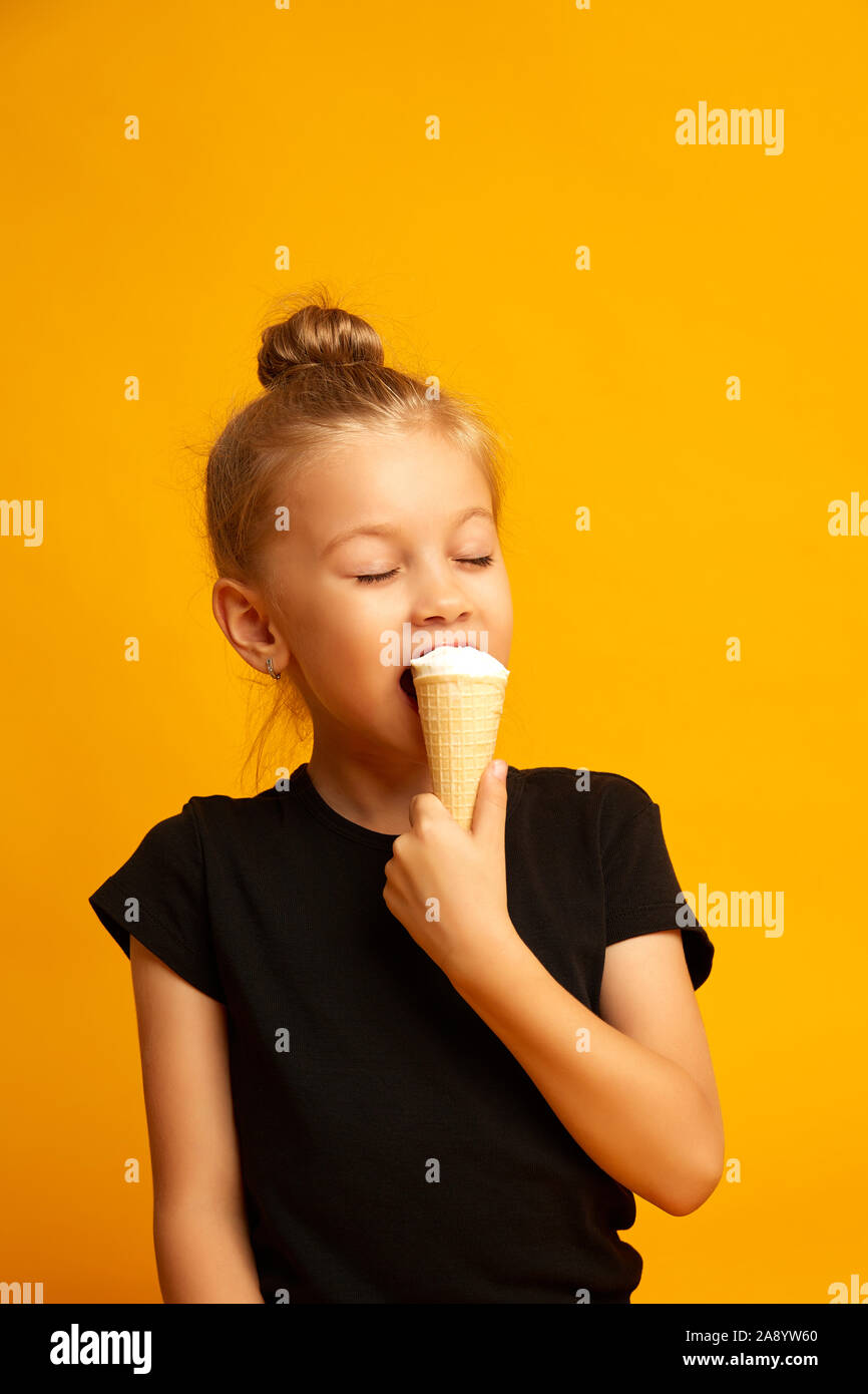 Little Ballerina in un costume da bagno con gli occhi chiusi mangia il gelato in un studio su sfondo giallo Foto Stock