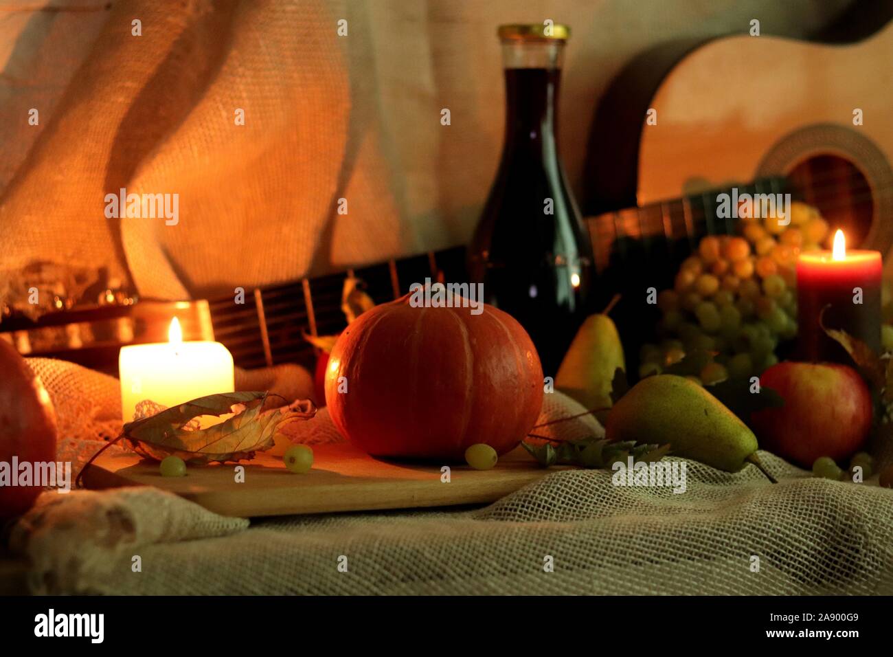 Ferma la vita raccolto di zucca, pere, mele, uva e candele luce morbida con una bottiglia di vino e la chitarra su un letto di sacco Foto Stock