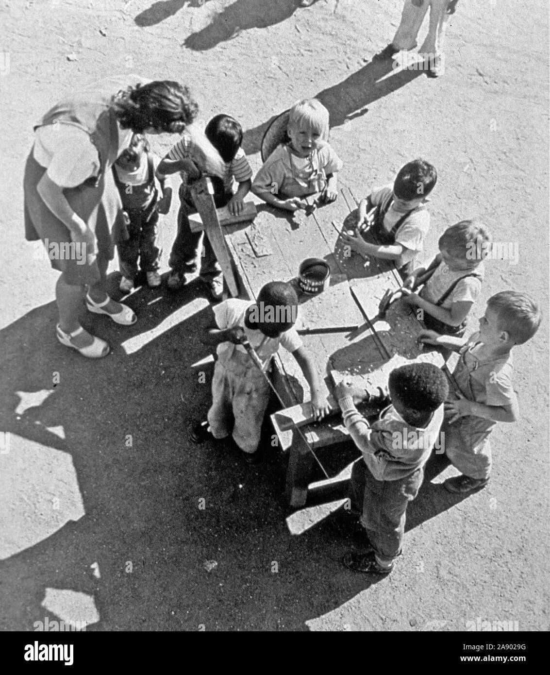 Vista aerea di diversi bambini che lavorano con seghe e martelli a una tabella in un area giochi all'aperto ca. 1950 Foto Stock