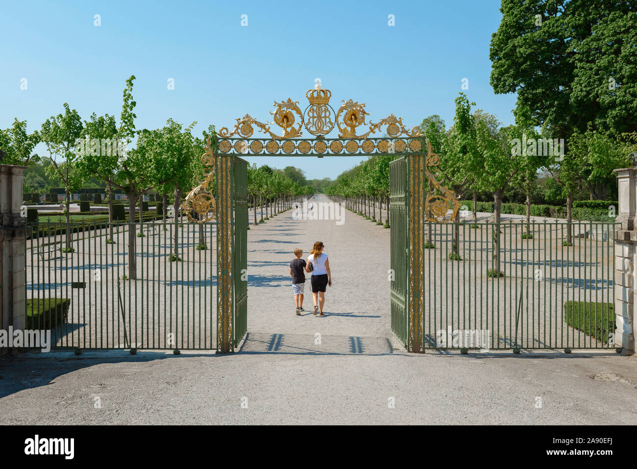 Madre figlio di viaggio, vista posteriore di un genitore e bambino di entrare nel giardino barocco del Castello di Drottningholm, residenza della famiglia reale svedese, Svezia. Foto Stock