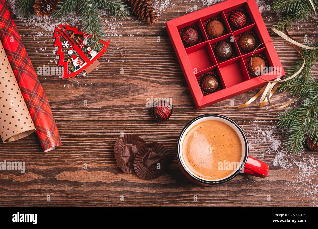 Cioccolatini in un rosso scatola craft tazza di una bevanda calda su un Natale in legno di abete di sfondo dei rami di un nuovo anno di giocattolo. Disposizione piatta vista dall'alto. Copia sp Foto Stock