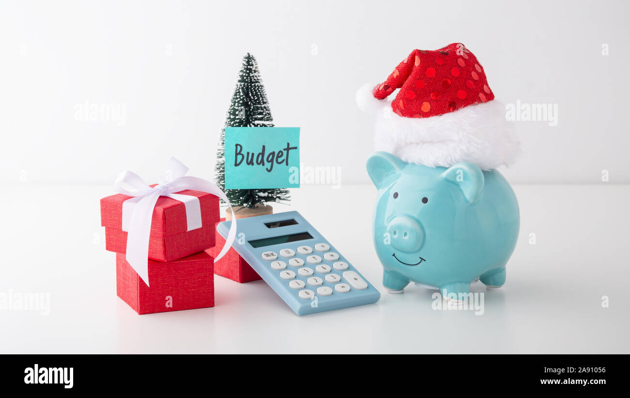 Bilancio di natale e il concetto di risparmio, salvadanaio con cappello di Natale, la decorazione e la calcolatrice sul tavolo bianco Foto Stock