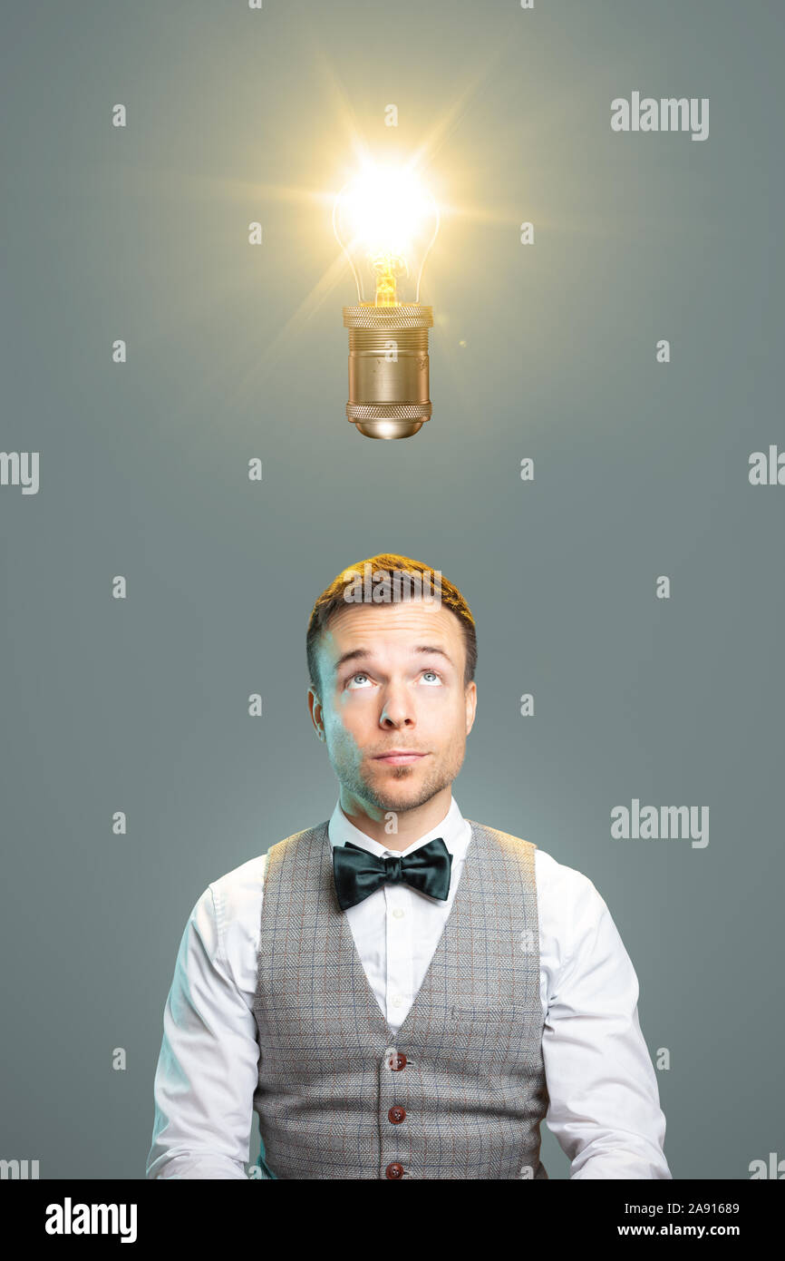 Uomo che guarda verso una lampadina sopra la sua testa Foto Stock