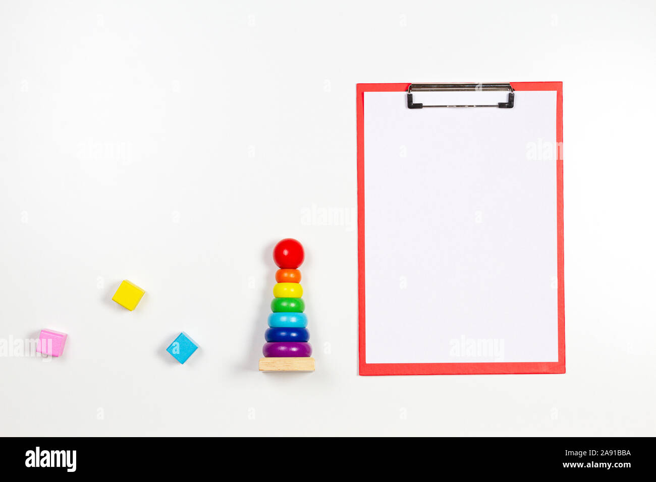 Colorato baby kid giocattoli e appunti rosso con foglio di carta bianco su sfondo bianco. Vista superiore Foto Stock