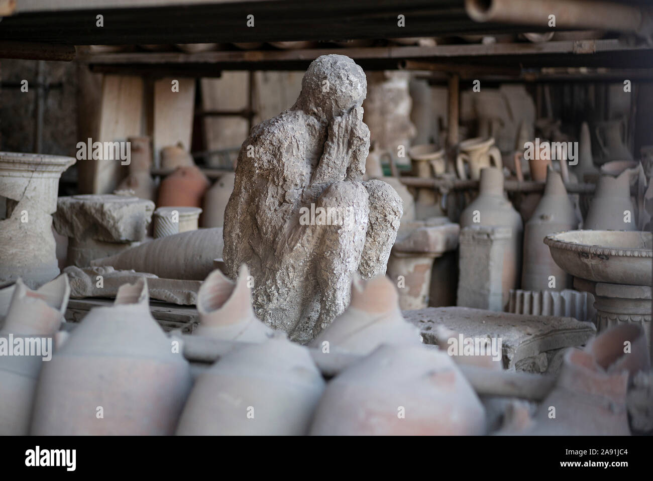 Pompei. L'Italia. Sito archeologico di Pompei. Calco in gesso di una vittima che morì in eruzione del Vesuvio nel 79 D.C., circondato da artefatti f Foto Stock