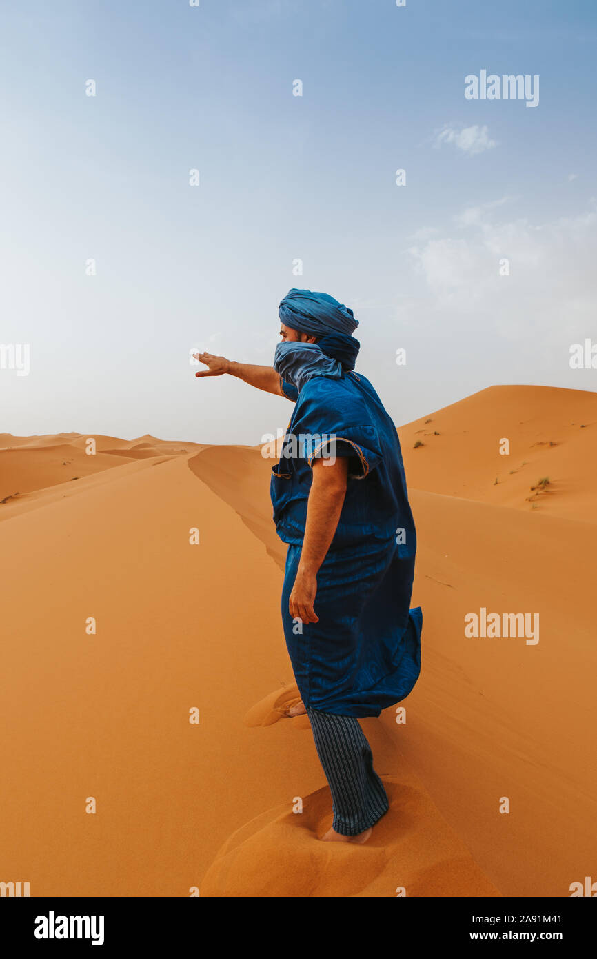 L'uomo con il classico riff vestiti in piedi e dispositivo di puntamento con la mano sulle dune del deserto da soli. Foto Stock