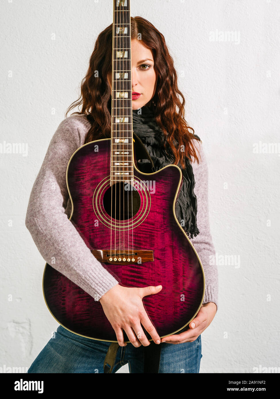Giovane bella donna redhead tenendo una chitarra acustica oltre il suo volto. Foto Stock
