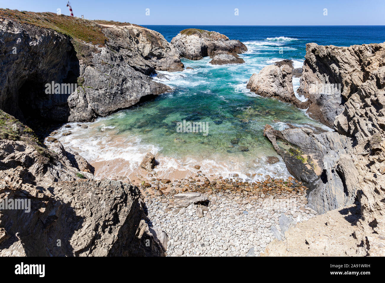 Bellissima spiaggia con pietre rotonde, protetta dalle onde da rocce lungo la strada dei pescatori nel Alentejo, del Portogallo, dell'Europa. Foto Stock