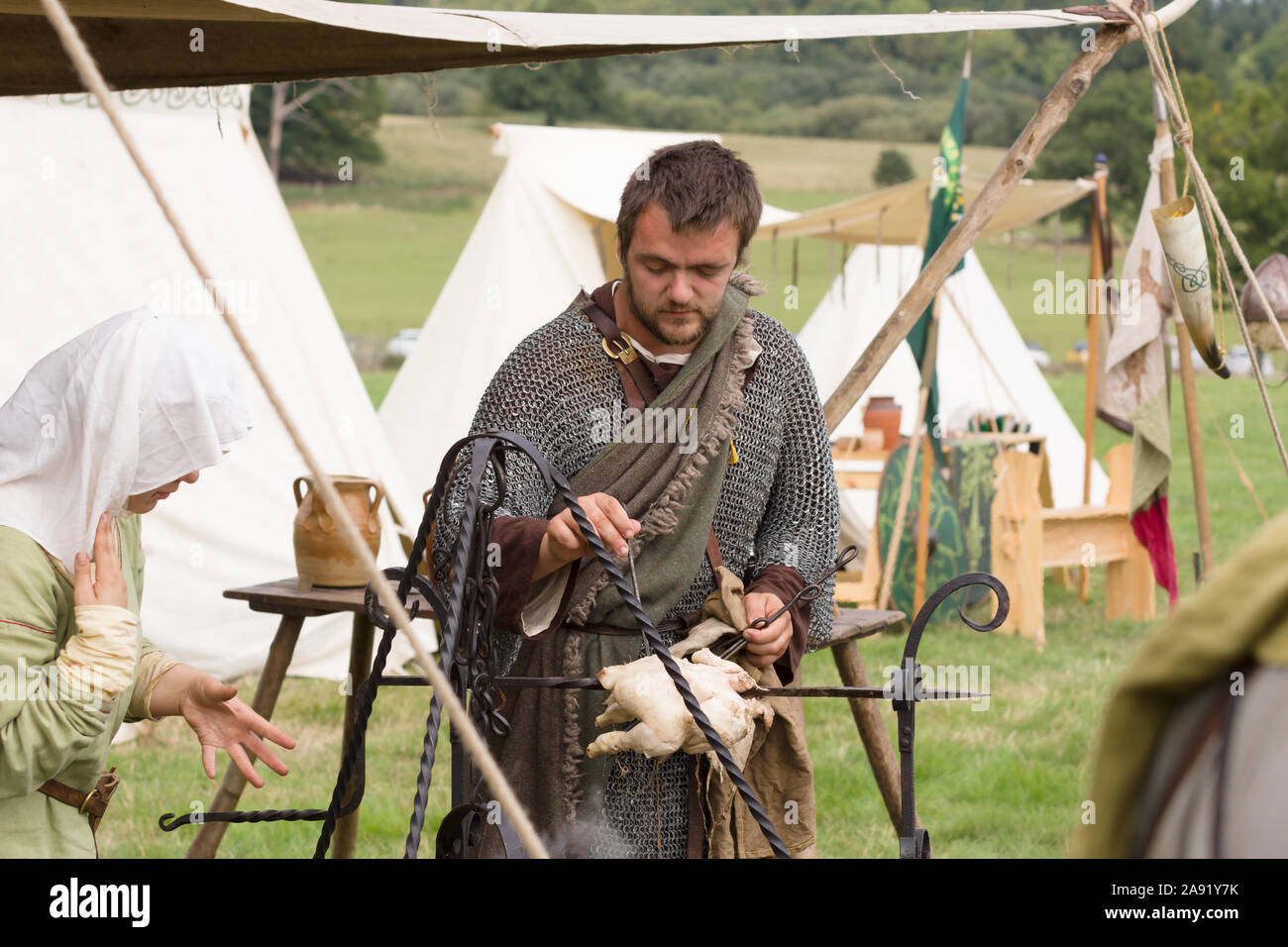 Uomo vestito in costume medievale la preparazione di cibo in una rievocazione camp Foto Stock