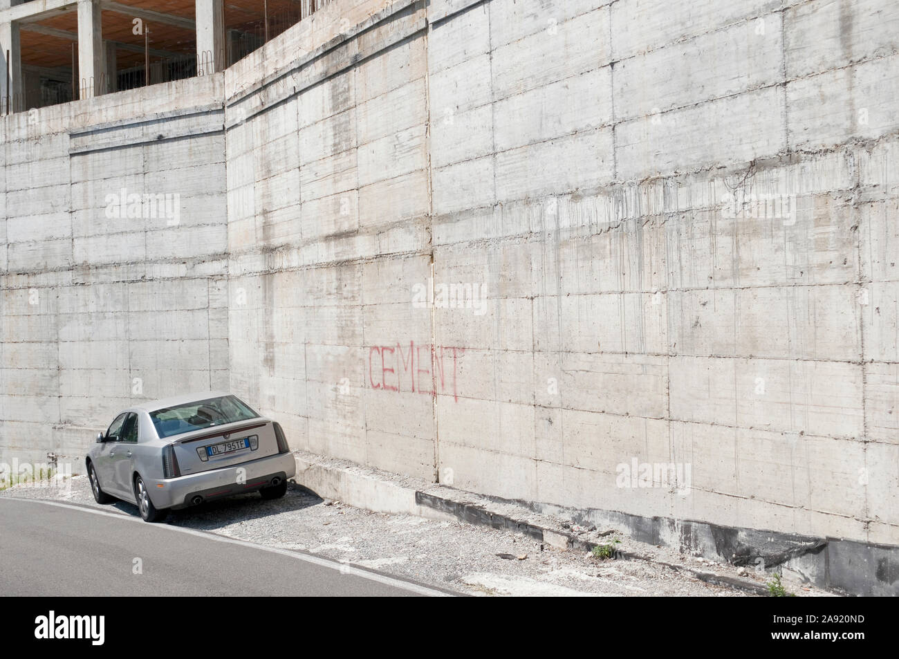 Macchina parcheggiata accanto al calcestruzzo corazzato muro di un edificio incompleto, Italia Foto Stock
