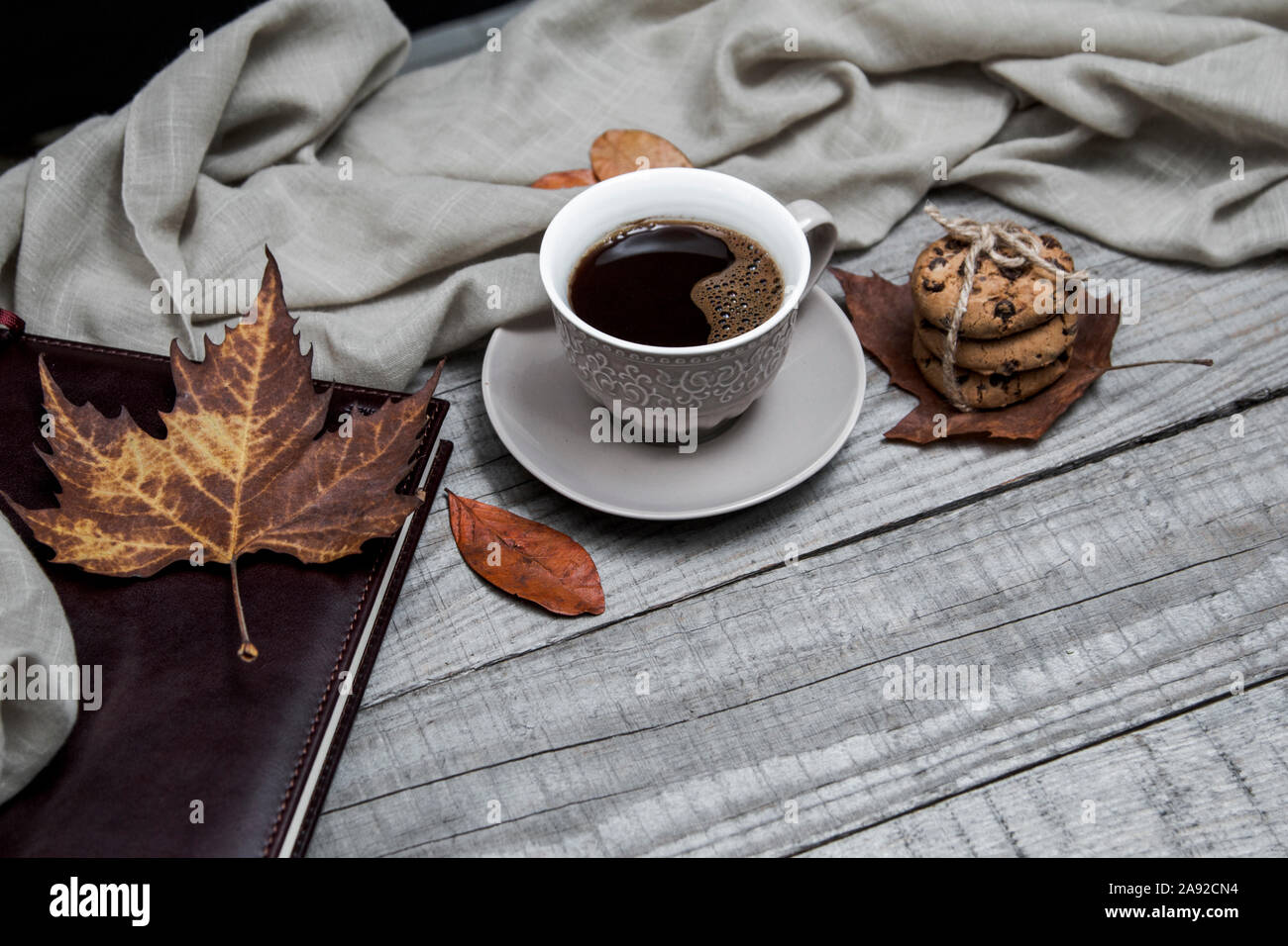 Tazza di caffè nero con biscotti al cioccolato circondato da foglie di autunno e portatile su una tavola di legno Foto Stock