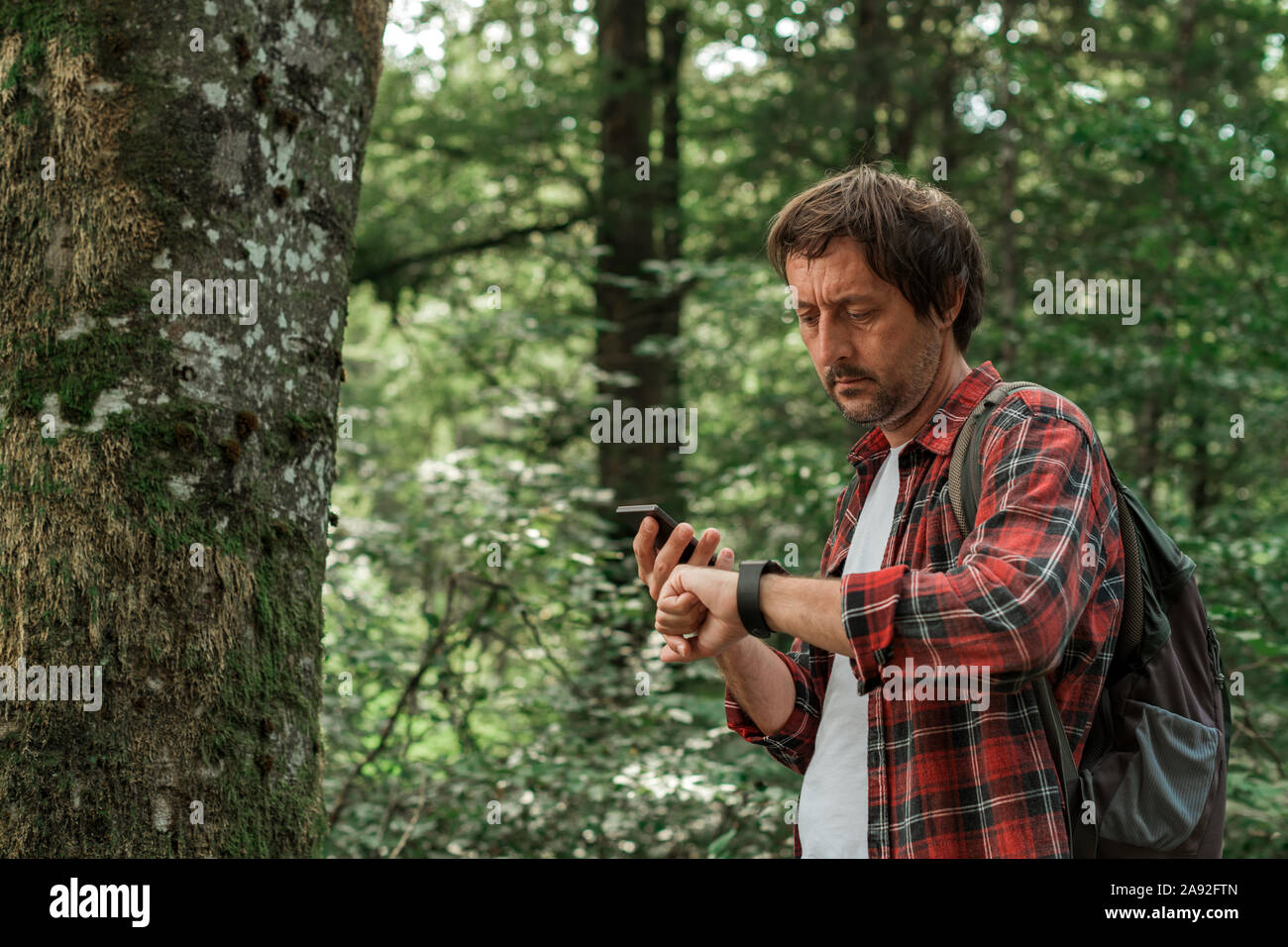 Escursionista smartwatch di collegamento allo smartphone per eseguire la sincronizzazione dei dati su dispositivi durante le escursioni nella foresta,fuoco selettivo Foto Stock