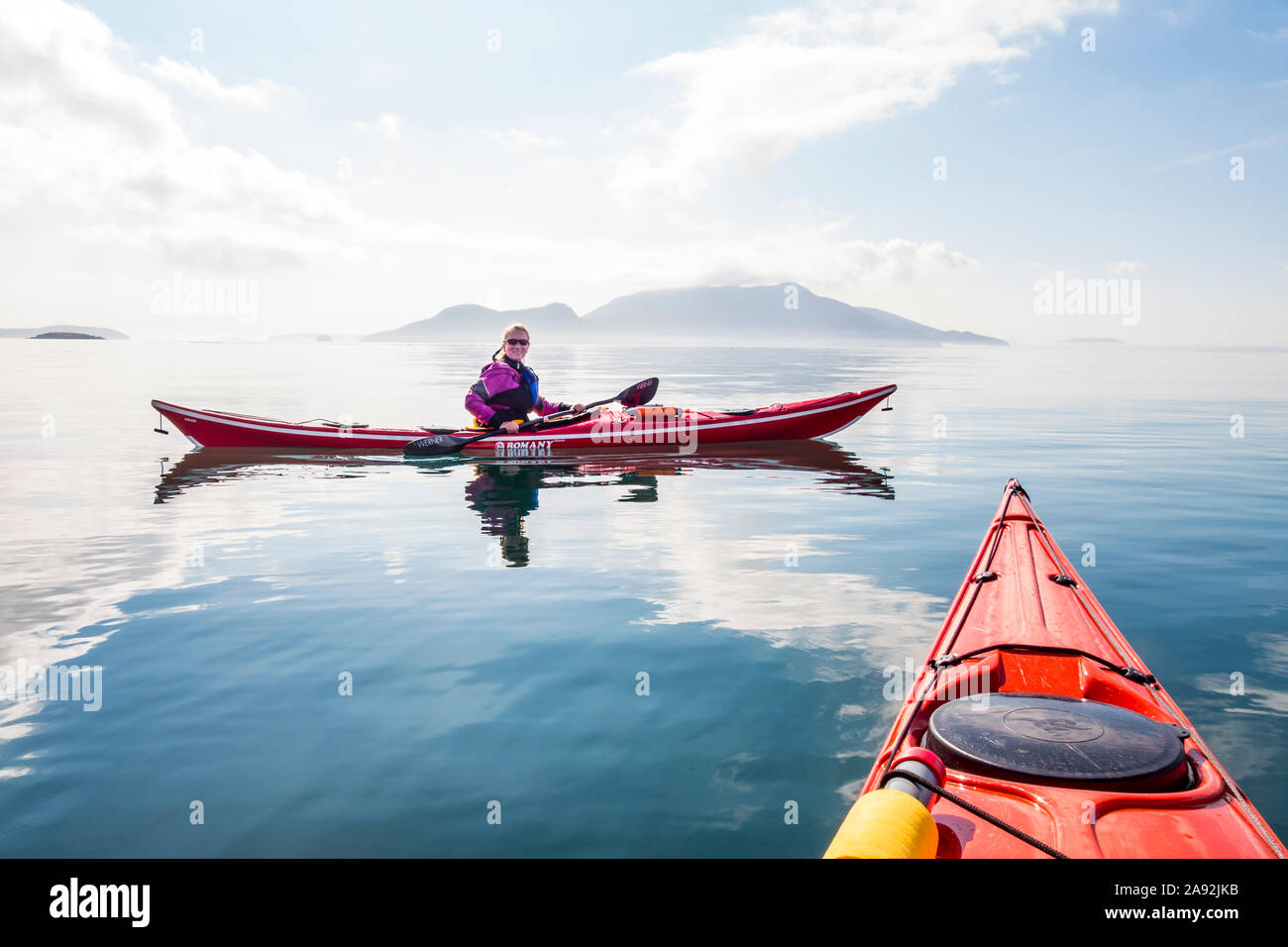 Un ritratto di una donna nel suo kayak di mare off southe la sponda  orientale di Orcas Island vicino Doe Bay, Rosario stretto, con i cipressi  isola sullo sfondo Foto stock -