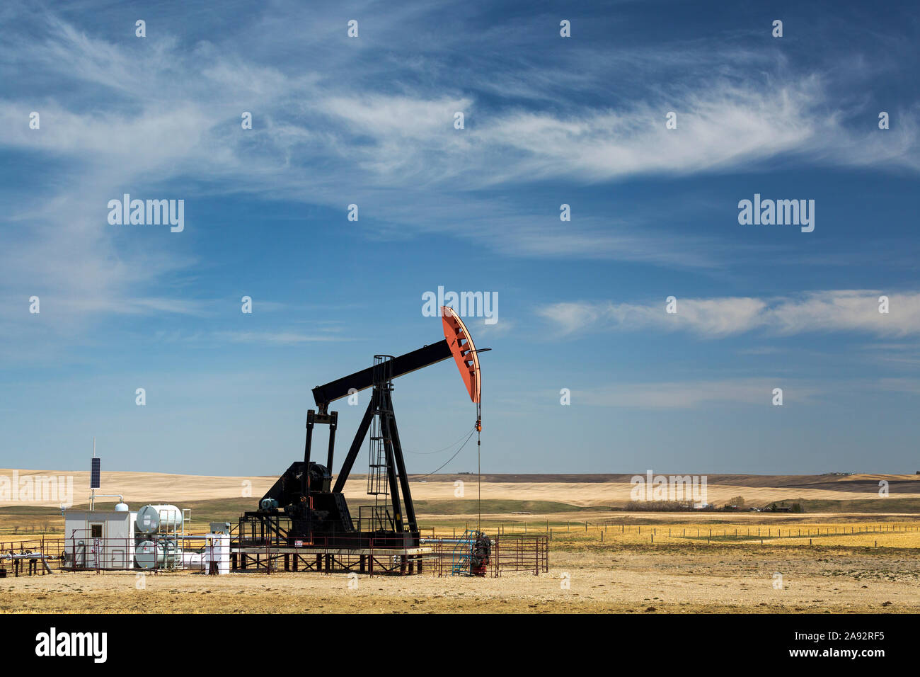 Pumpjack in campo con colline ondulate, nuvole e cielo blu sullo sfondo, ad ovest di Airdrie; Alberta, Canada Foto Stock