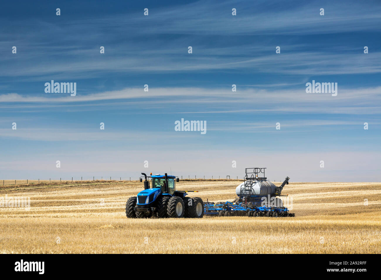 Trattore con seminatrice pneumatica, semina un campo stoppia con cielo blu e nuvole frizzanti, vicino a Beiseker; Alberta, Canada Foto Stock