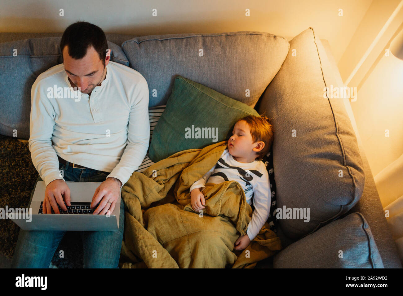 Padre utilizzando laptop in salotto mentre la figlia di dormire vicino a lui Foto Stock