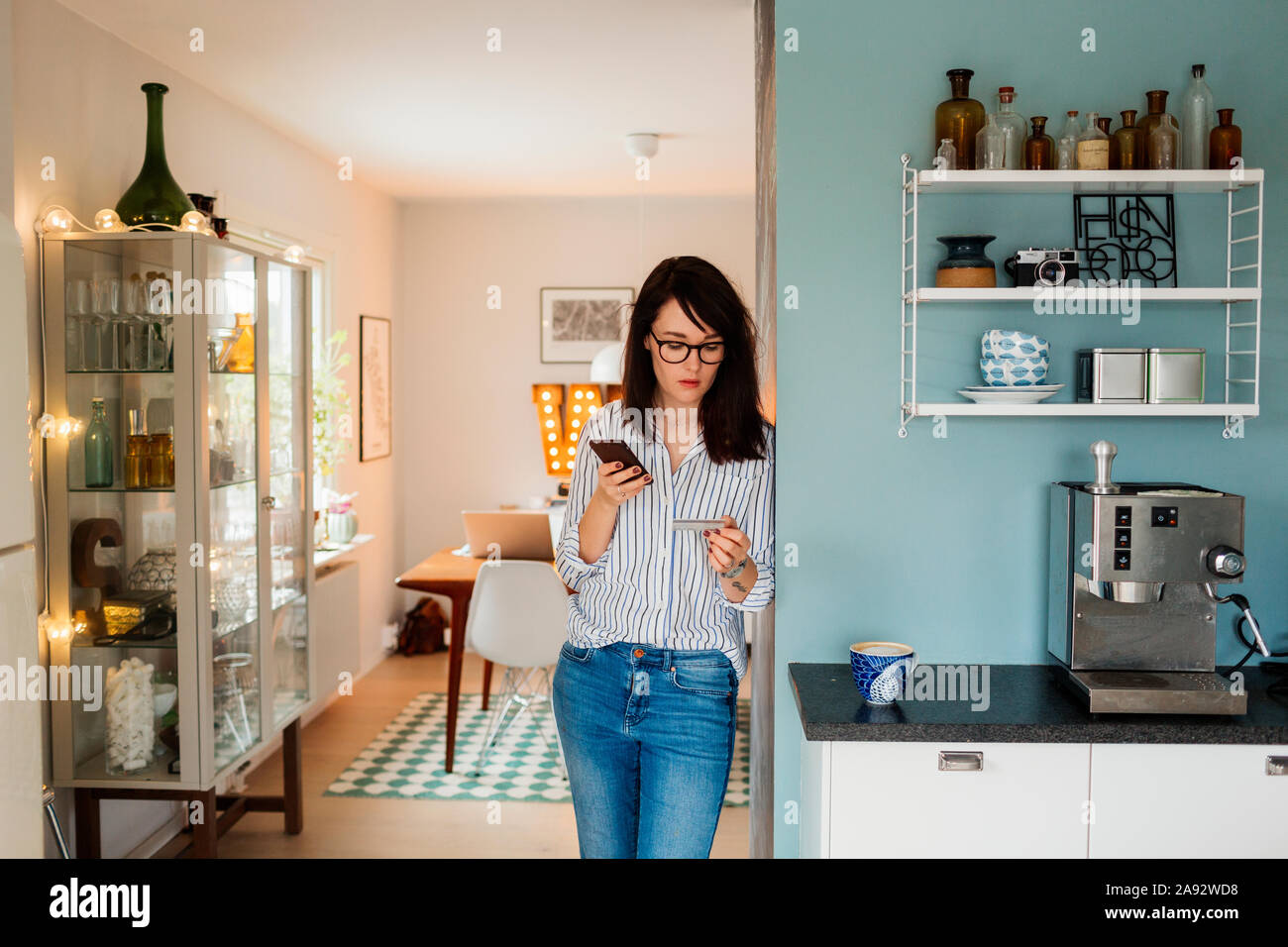 Giovane donna con lo smartphone e la carta di credito in cucina Foto Stock