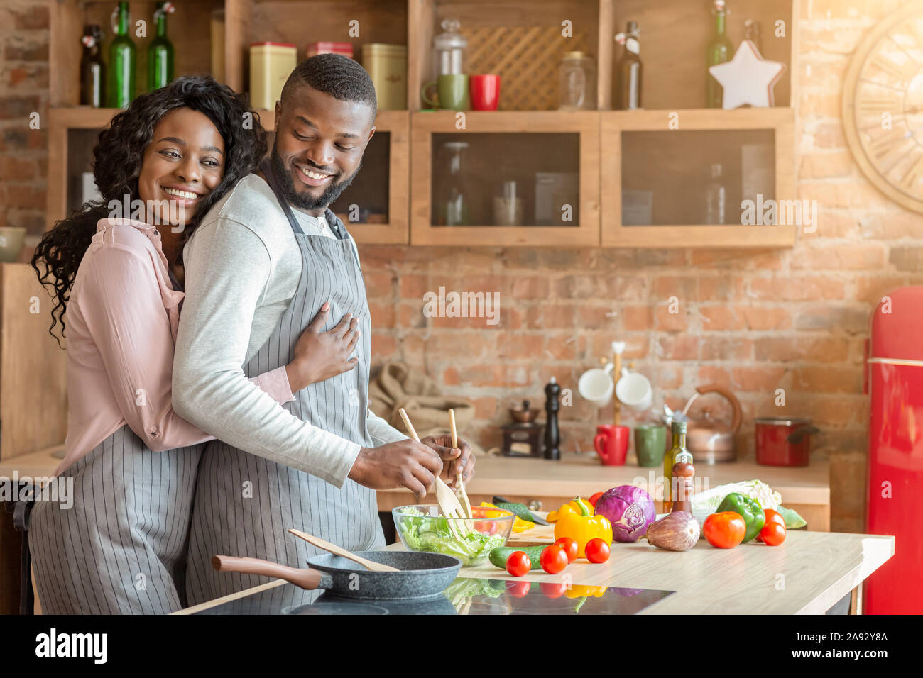 Grati moglie abbracciando il marito da dietro in cucina Foto Stock