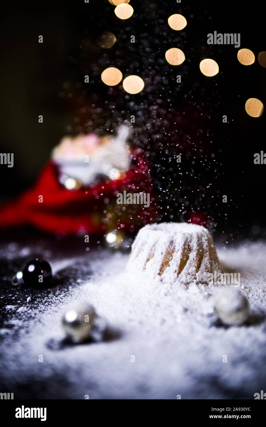 Caldo Natale a casa con un dolce mini bundt cake, lo zucchero in polvere cade sopra un caldo caldo bundt mini torta con ornamento di Natale e un boccale di sfocati Foto Stock