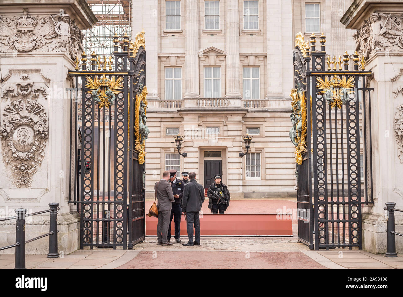 Guardando attraverso le porte aperte di fronte a Buckingham Palace, nel centro di Londra, Regno Unito. Polizia armata sulla guardia di controllo della sicurezza dei visitatori. Guardia famiglia reale. Foto Stock