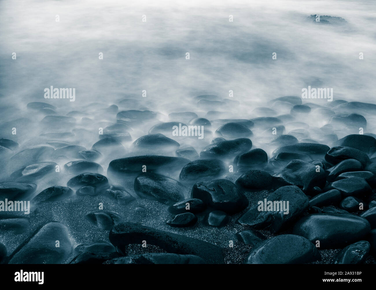 Una lunga esposizione delle onde che si infrangono sulle rocce sulla spiaggia. Foto Stock