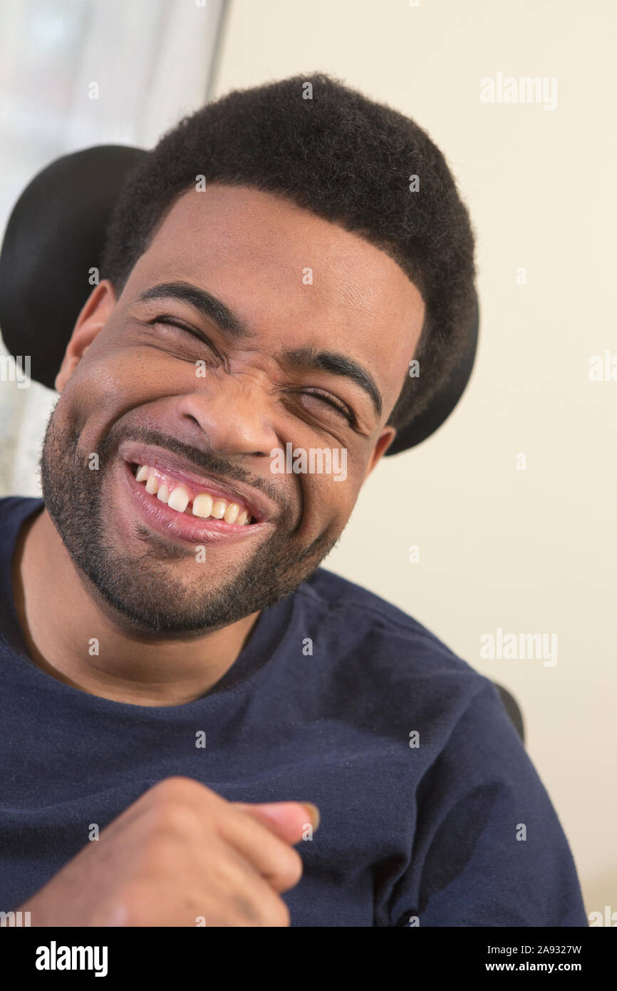 Ritratto di felice afroamericano con la paralisi cerebrale sorridente su sedia a rotelle a casa Foto Stock