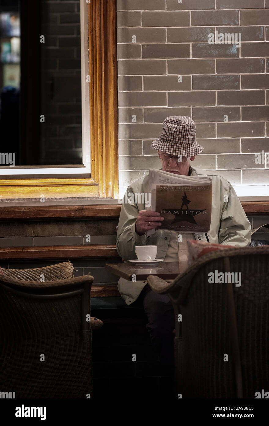 Uomo che legge il giornale e bere il tè nel cafè al baratto libri, Alnwick, Northumberland, Regno Unito Foto Stock