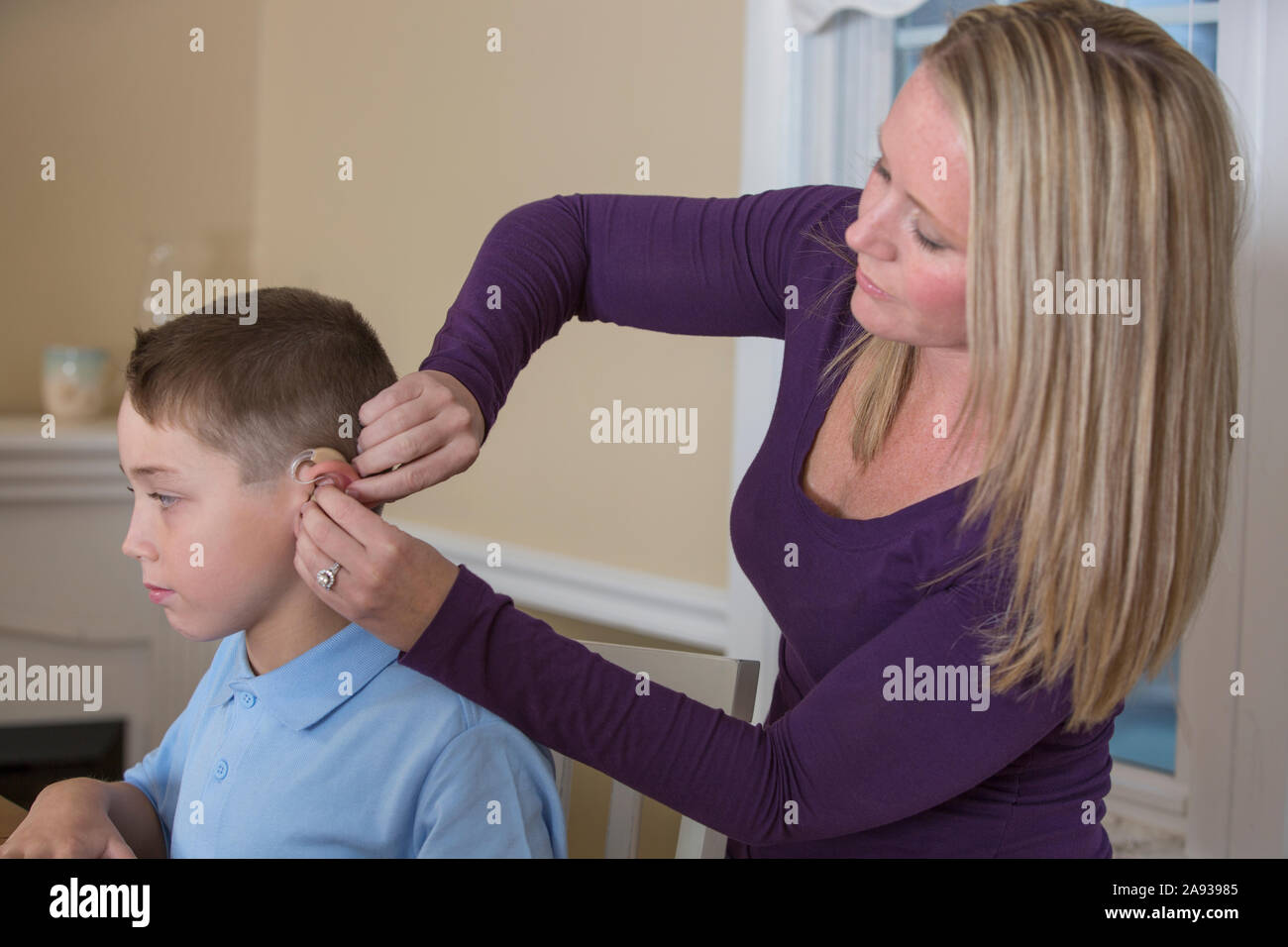 Madre che mette un apparecchio acustico su suo figlio con un compromissione dell'udito a casa Foto Stock